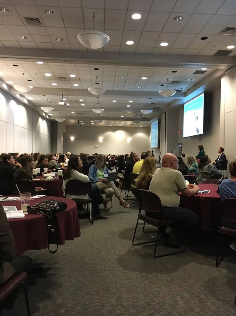 A large conference room filled with hundreds of attendees watches a pediatric microtia presentation projected on a screen at the front of the room. Dr. Arturo Bonilla regularly speaks at medical conferences to educate healthcare professionals about microtia surgery and ear reconstruction.