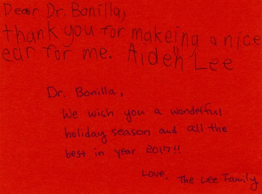 Tarjeta navideña roja escrita a mano por Aiden Lee, que agradece al Dr. Arturo Bonilla haberle hecho una bonita oreja, firmada con cariño por la familia Lee para la temporada de 2017: un emotivo regalo de agradecimiento al Dr. Arturo Bonilla de un paciente agradecido que se sometió a cirugía de microtia
