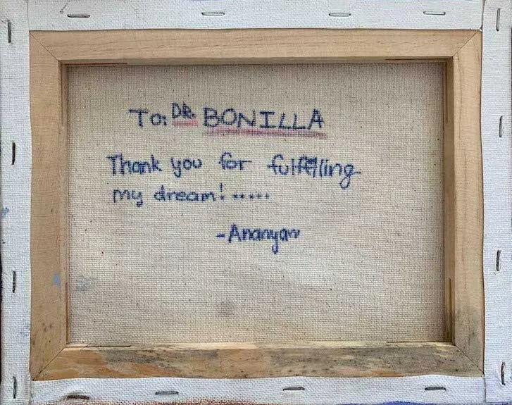 Reverso de un lienzo montado con la inscripción «Para el Dr. Bonilla. Gracias por cumplir mi sueño», firmada por Ananyav: la dedicatoria personal escrita detrás de una pintura original regalada al Dr. Arturo Bonilla por un paciente agradecido que se sometió a cirugía de microtia