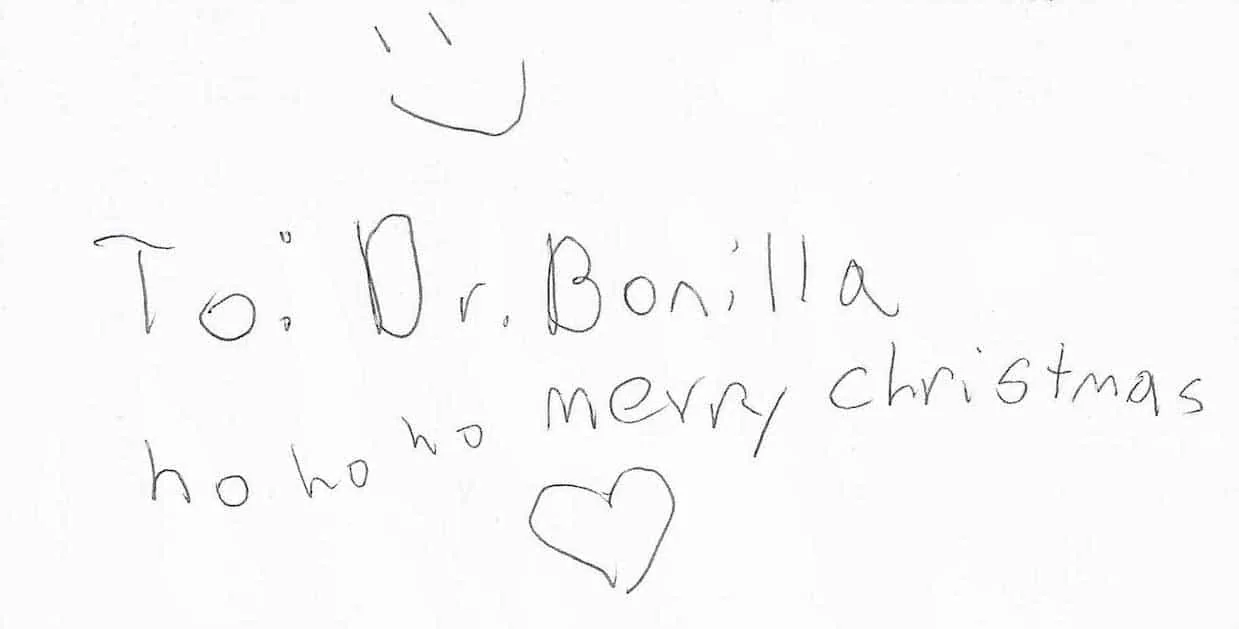 Tarjeta navideña sencilla escrita a lápiz, dirigida al Dr. Arturo Bonilla, que dice «jo, jo, jo, feliz Navidad», con un pequeño dibujo de un gorro de Papá Noel y un corazón: una dulce nota artesanal por la celebración de un paciente joven que se sometió a cirugía de microtia