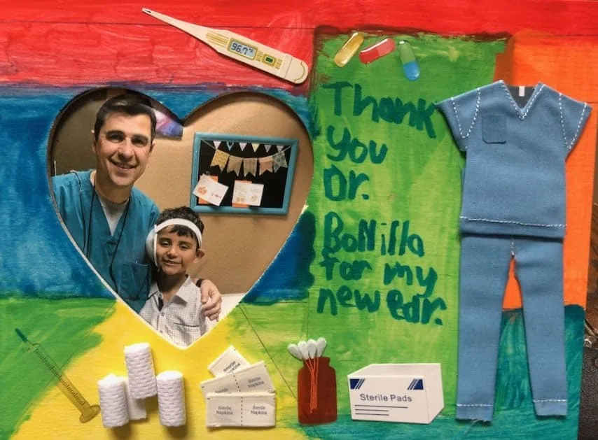 Collage artesanal de técnica mixta con una fotografía en forma de corazón del Dr. Arturo Bonilla junto a un paciente vendado con microtia, rodeada de un recorte de tela de ropa quirúrgica y materiales médicos reales, con el mensaje «Gracias, Dr. Bonilla, por mi nueva oreja»: un regalo creativo de agradecimiento de un paciente agradecido que se sometió a cirugía de microtia