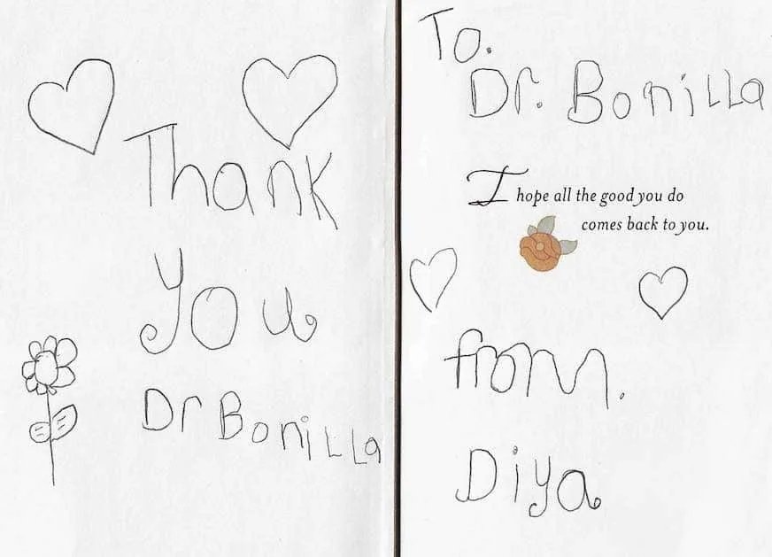 Tarjeta infantil plegada y escrita a mano de una paciente llamada Diya, con corazones y una flor dibujados a lápiz y el mensaje «Gracias, Dr. Bonilla. Espero que todo el bien que hace vuelva a usted»: un delicado y considerado regalo de agradecimiento de una paciente agradecida que se sometió a cirugía de microtia