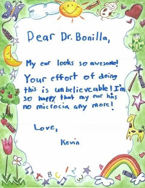 Carta escrita en azul sobre papel decorativo preimpreso por un niño llamado Kevin, que celebra que su oreja se ve increíble y declara que ya no tiene microtia, enviada al Dr. Arturo Bonilla después de una cirugía exitosa de reconstrucción de oreja por microtia: una nota entusiasta de un paciente joven y alegre