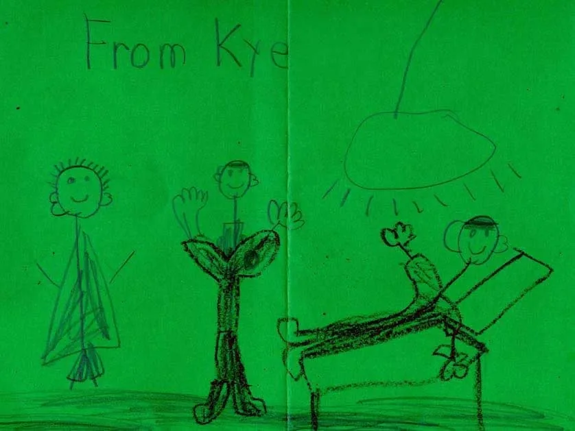Dibujo infantil con crayones sobre papel verde, de un paciente llamado Kye, que muestra tres escenas de figuras de palitos, incluida la de un niño sobre una camilla de exploración, con un sol y una nube encima: un dulce regalo de agradecimiento al Dr. Arturo Bonilla de un paciente agradecido que se sometió a cirugía de microtia