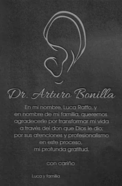 Elegante tarjeta de fondo oscuro dirigida al Dr. Arturo Bonilla, con una refinada ilustración lineal de una oreja y una dedicatoria en español de Luca Raffo y su familia, que le agradecen haber transformado la vida de Luca mediante el don de Dios de su habilidad quirúrgica: un homenaje sofisticado y profundamente agradecido de un paciente internacional que se sometió a cirugía de microtia