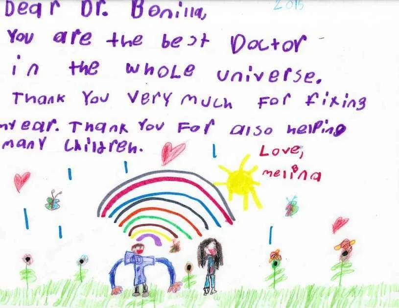 Carta de 2015 escrita con lápiz morado por una niña llamada Melina, ilustrada con un arcoíris, un sol, dos figuras, mariposas y corazones, que agradece al Dr. Arturo Bonilla haberle arreglado la oreja y ayudar a muchos niños: un alegre regalo de una paciente agradecida que se sometió a cirugía de microtia