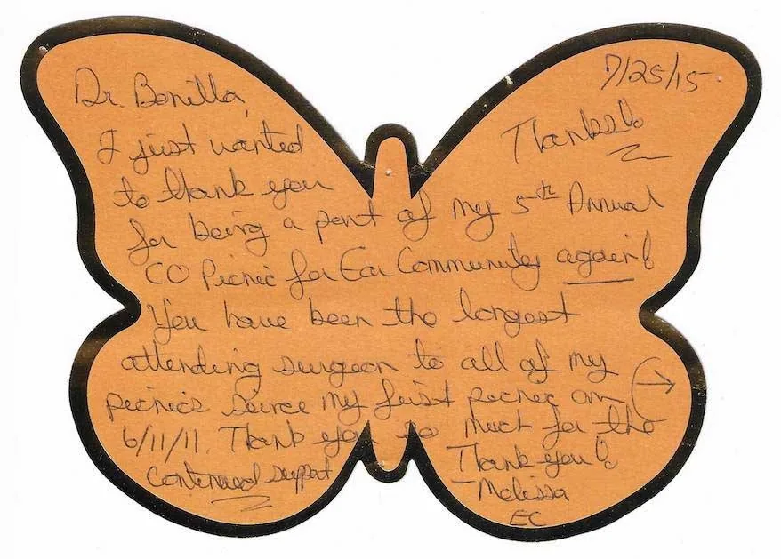 Nota manuscrita en una tarjeta naranja con forma de mariposa, fechada 7/25/15, de Melissa de Ear Community, que agradece al Dr. Arturo Bonilla ser el cirujano que lleva más tiempo asistiendo a su pícnic anual desde la primera reunión del 6/11/11: un homenaje comunitario único que honra su dedicación continua a los pacientes que se someten a cirugía de microtia