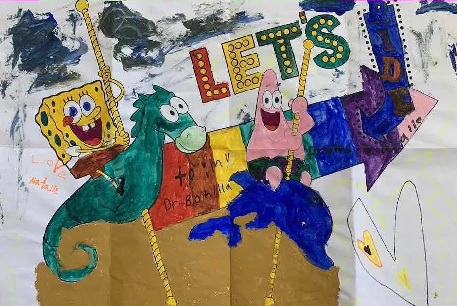 Dibujo grande y colorido de una niña llamada Natalie, con SpongeBob, Patrick Star y criaturas marinas en un carrusel, con las palabras «Vamos a dar una vuelta», dedicado al Dr. Arturo Bonilla: un regalo imaginativo y alegre de una paciente agradecida que se sometió a cirugía de microtia