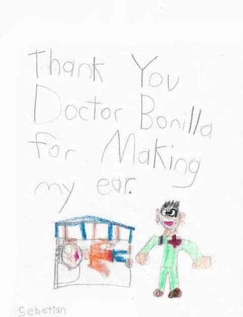 Dibujo infantil de Sebastian para el Dr. Bonilla, que muestra al doctor de pie junto a un paciente en una cama de hospital, con un mensaje que le agradece haberle hecho la oreja