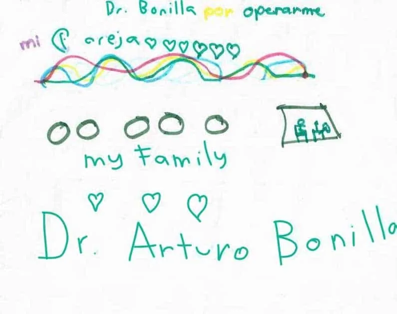 Dibujo infantil en tinta verde dirigido al Dr. Arturo Bonilla, con líneas onduladas de colores, corazones, figuras circulares rotuladas «mi familia» y el nombre completo Dr. Arturo Bonilla escrito en letras grandes, que le agradece en español haberle operado la oreja: un regalo vivo y cariñoso de un paciente joven que se sometió a cirugía de microtia