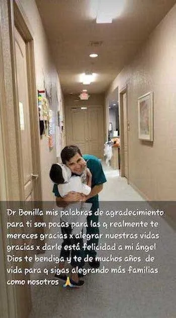 Fotografía del Dr. Arturo Bonilla con ropa quirúrgica, inclinándose para abrazar a un niño pequeño en el pasillo de una clínica, con un mensaje superpuesto en español que expresa que las palabras no pueden transmitir la gratitud por haberle dado alegría al ángel de su familia: un agradecimiento profundamente emotivo al Dr. Arturo Bonilla de la familia de un paciente agradecido que se sometió a cirugía de microtia