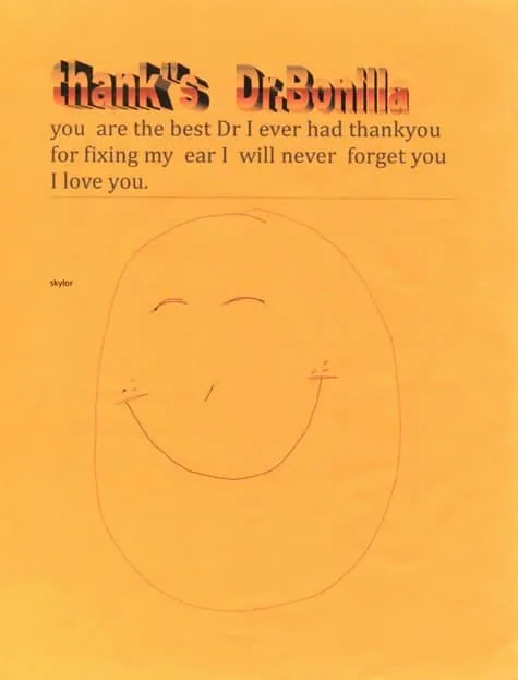 Carta de agradecimiento escrita a mano al Dr. Bonilla por la cirugía de oreja por microtia, con una gran cara sonriente naranja dibujada a mano y un mensaje de gratitud de un paciente llamado Skylor