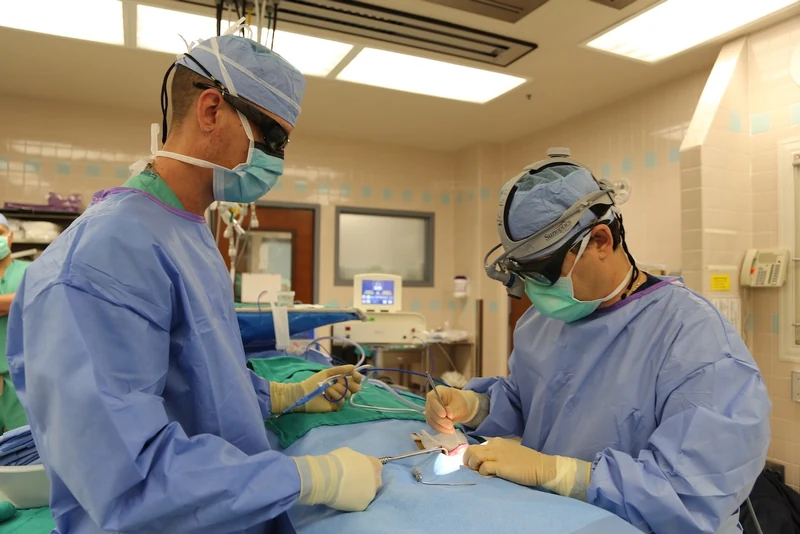 Dr. Arturo Bonilla performing microtia ear reconstruction surgery in the operating room in San Antonio, using precision surgical instruments and magnification loupes to hand-carve the rib cartilage ear framework.