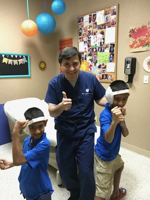 Dr. Arturo Bonilla poses with twin brothers from India, both born with bilateral microtia, celebrating the completion of their ear reconstruction surgery at his San Antonio office — one of over 50 countries represented in his practice.