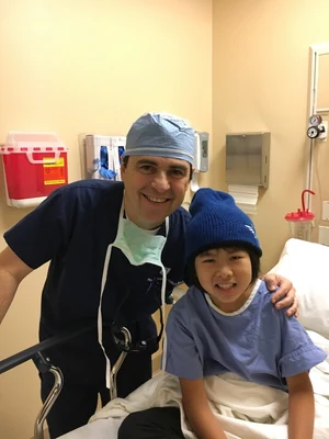 Dr. Arturo Bonilla with a young microtia patient who traveled from China for ear reconstruction surgery, photographed together in the hospital in San Antonio after a successful procedure.